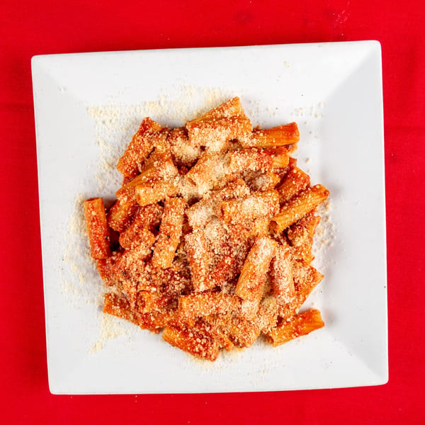Rigatoni pasta with red sauce and generous grated Parmesan cheese on a white plate.