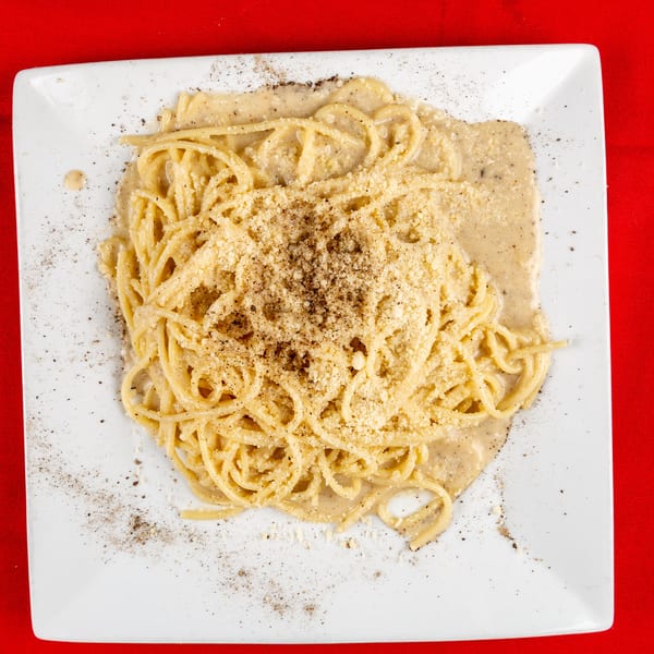 Spaghetti with creamy sauce, grated cheese, and black pepper on a white plate, against a red background.