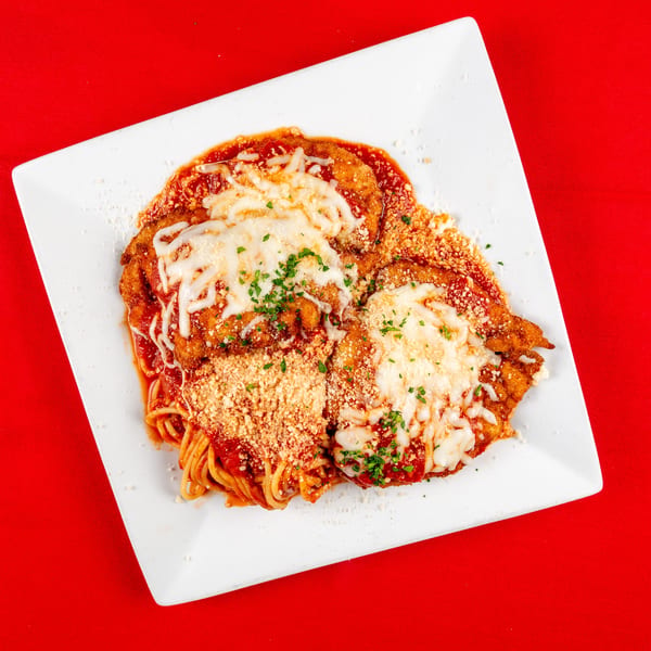 Two chicken parmesan cutlets with spaghetti, marinara, mozzarella, and grated parmesan on a white plate.