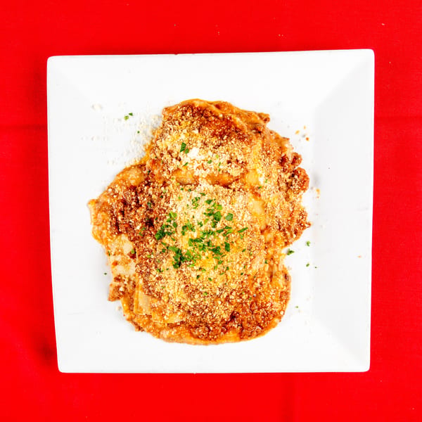 Overhead view of baked pasta with red sauce, parmesan, and parsley on a white plate.