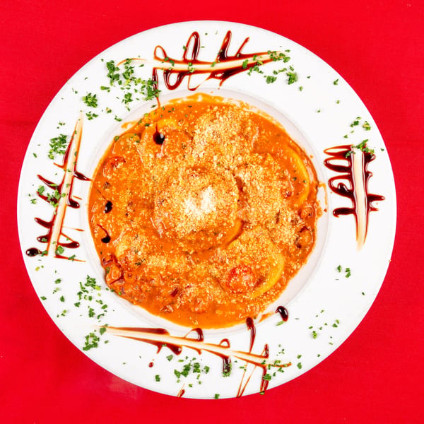 Ravioli in a creamy tomato sauce, topped with parmesan, parsley, and balsamic glaze on a white plate.